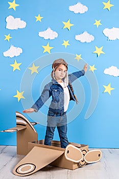 Little child girl in a pilot`s costume is playing and dreaming of flying over the clouds.