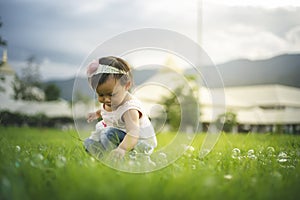 Little child girl playing with bubbles on green grass outdoors in the park