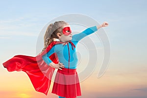 Little child girl plays superhero. Child on the background of sunset sky.