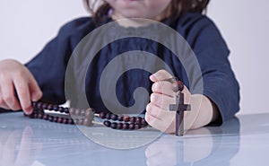 Little child girl praying and holding a wooden rosary as symbol of belief and faith in Jesus Christ and eternal life