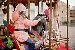 Little child girl riding a wooden horse on a carousel at Christmas funfair.