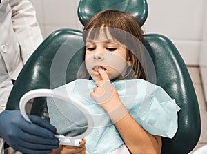 Little child Girl seating in dental office and looking at her teeth the mirror
