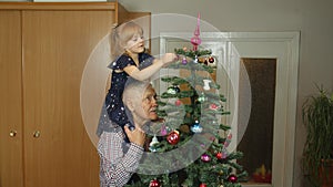 Little child girl with senior grandparent decorating artificial Christmas tree at old-fashion home