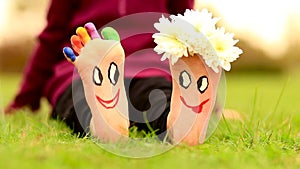 Little child girl sits on grass with painted feet with funny comic faces