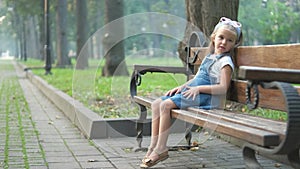 Little child girl sitting alone on a bench in summer park