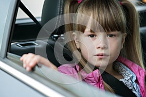 Little child girl sitting in a car on rear seat fastened with safety belt