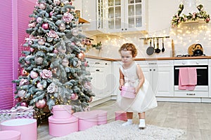 Little child girl staying in the kitchen decorated for Christmas and holding gift box