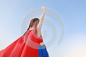 Little child girl Superhero in a gesture to fly on clear blue sky background. Kid super hero concept