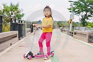 Little child girl to ride scooter in outdoor sports ground on sunny summer day. Active leisure and outdoor sport for children