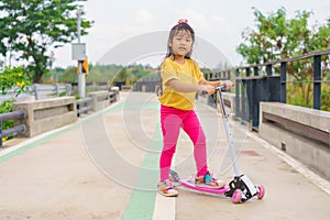 Little child girl to ride scooter in outdoor sports ground on sunny summer day. Active leisure and outdoor sport for children