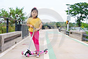 Little child girl to ride scooter in outdoor sports ground on sunny summer day. Active leisure and outdoor sport for children