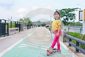 Little child girl to ride scooter in outdoor sports ground on sunny summer day. Active leisure and outdoor sport for children