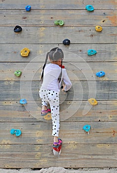 Little child girl trying on free climbing on the playground wooden wall outdoors