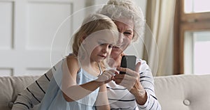 Little child girl using mobile phone with smiling elderly grandmother.