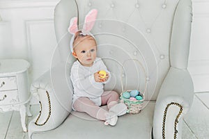 Little child girl wearing bunny ears on Easter day and playing with painted eggs