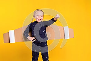 A little child girl is wearing homemade cardboard flying wings, pretending to be a pilot for a craft, imagination or