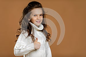 Little child girl in white sweater showing thumbs up