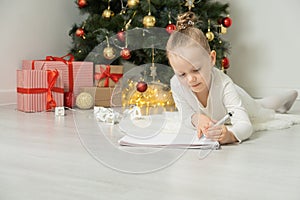 Little child girl writes letter to Santa Claus and dreams of a gift background Christmas tree.