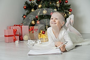 Little child girl writes letter to Santa Claus and dreams of a gift background Christmas tree.