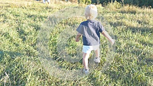 Little child goes on green grass at the field to his father at sunny day. Happy family on a summer meadow. Baby boy