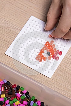 Little child hands make beads art in the shape of a fish