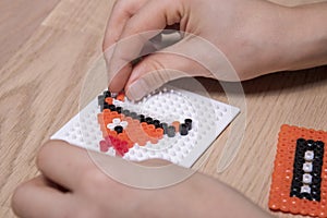 Little child hands make beads art in the shape of a fish.