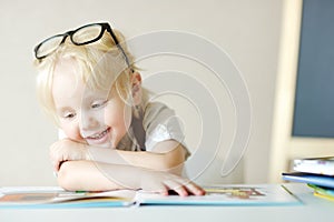 Little child is having fun with a book. Cute boy is watching pictures and learning letters. Preparation for school, early