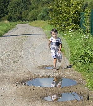 Little child having fun by running and jumping the puddle