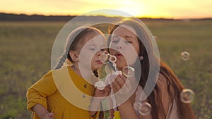 little child with her mother blowing soap bubbles at sunset, girl daughter with mom play fun outdoors together, happy