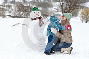 Little child and her Young mother next to large snowman have fun. Winter weekend with the family outside the city