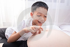 little child holding the belly of a pregnant mother. Pregnant mother and son are happy. little boy looking at her mother's