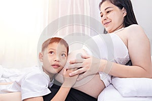 little child holding the belly of a pregnant mother. Pregnant mother and son are happy. little boy looking at her mother's