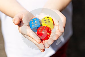 Little child holding three colorful wooden dice showing six in her small hands, closeup. Multi colored game dice with number 6