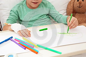 Little child with infusion drip drawing in hospital bed