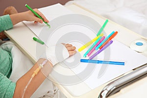 Little child with infusion drip drawing in hospital bed