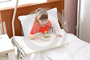 Little child with intravenous drip eating soup in bed