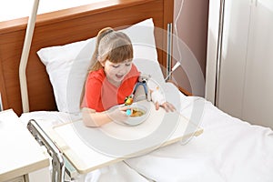 Little child with intravenous drip eating soup in hospital