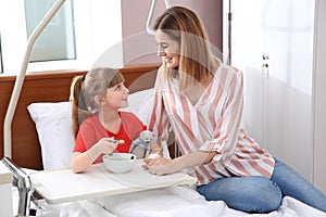 Little child with intravenous drip eating soup in hospital bed