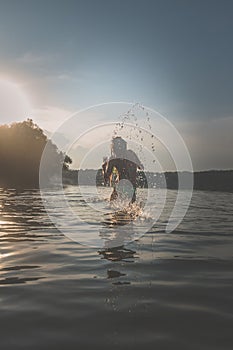 Little child jumping and splashing water in rural pond in beautiful colorful sunset