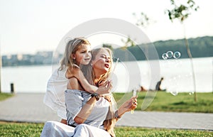 Little child keeps wondering. Photo of young mother and her daughter having good time on the green grass with lake at