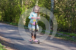 Little child learning to ride a scooter in a city park on sunny summer day. Kids play outdoors. Active leisure and outdoor sport