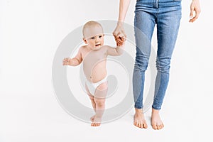 Little child learns to walk with the help of the mother, on a white background