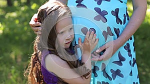 Little child listening baby in belly of her mother outdoor in sunny nature.