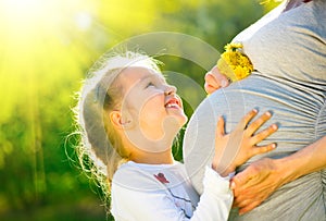 Little child listening baby in belly of her mother outdoor in sunny nature. Happy pregnant mother with her little daughter