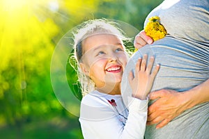 Little child listening baby in belly of her mother outdoor in sunny nature. Happy pregnant mother with her little daughter