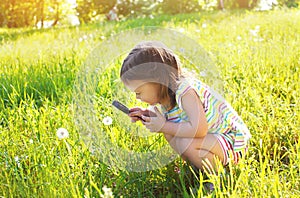 Little child looking through a magnifying glass on dandelion