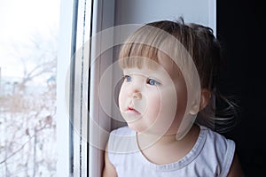 Little child looking out window. baby girl wanting to walk outdoors at rainy weather