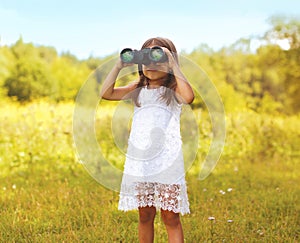 Little child looks in binoculars outdoors in sunny summer day