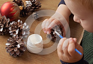 A little child makes decorations for Christmas from natural pine cones