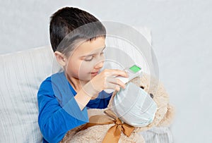 Little child measure temperature for toy bear in anti pollution mask with infrared modern digital thermometer